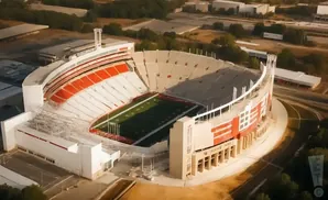 Aerial view of a large, open-air football stadium with red and white seating and a green field.