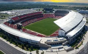 Aerial view of a large, red-seated stadium with a green field and a white, curved roof.