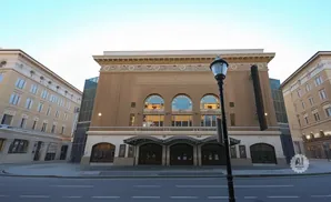 Theater with arched windows, brick facade, and ornate details, flanked by beige buildings under a clear sky.