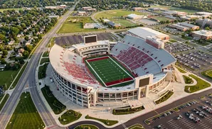 Aerial view of a large, open-air football stadium with red seating and a green field.