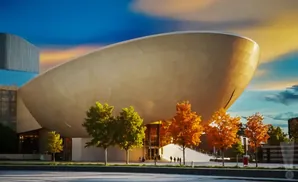 A modern, tan, ovular building with trees in front during sunset.