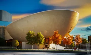 Modern building with a large, curved beige facade and fall trees in front.