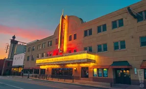 Sunset over an art deco movie theater with a bright marquee and neon sign.