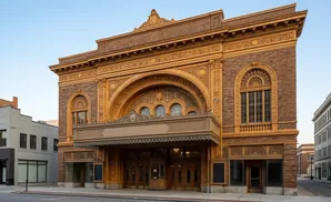 An ornate theater with brown brick and gold detailing, featuring a marquee and arched windows.