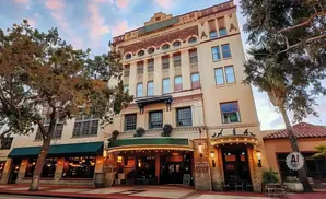 A historic building with ornate details and arched windows, featuring trees and a palm tree.
