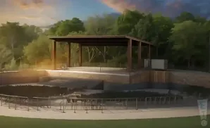 Outdoor amphitheater with a covered stage and tiered seating surrounded by trees under a sunset sky.