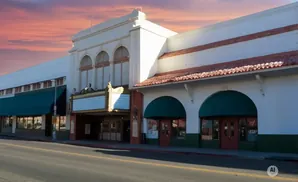 Exterior of a historic movie theater with a marquee, arches, and red tile roof under a sunset sky.