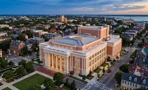 An aerial view of a large, salmon-colored building with columns, surrounded by historic homes and trees, at dusk.