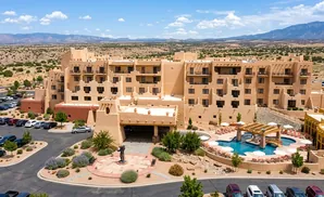 Aerial view of a tan, multi-story hotel with southwestern architecture, featuring a pool and parking lot.