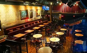 Interior of a dimly lit venue with brick walls, booth seating, and many tables and chairs.