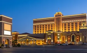 A large, illuminated casino resort glows orange and gold against a twilight blue sky.