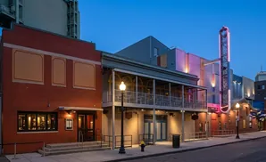 Night view of a brick building with a theater marquee and balconies, lit by streetlights and neon signs.
