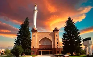 A mosque with a tall minaret stands against a dramatic sunset sky with vibrant orange and pink clouds.