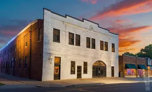 A brick building painted white with black trim stands against a colorful sunset sky.