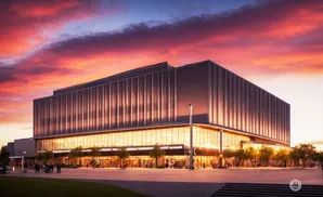 A modern building with a glass-fronted lower level and vertical panels on the upper level, set against a dramatic sunset sky.