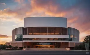 Modern building with rounded sections and large windows against a colorful sunset sky.