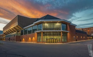 a hyper-realistic wide-angle aerial photograph of cross insurance arena in portland, maine, captured at sunset with the golden light highlighting the venue’s brick and glass façade. 