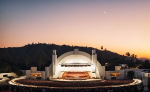 the hollywood bowl in los angeles, california at sunset. there is a crowd watching a concert, and you can see city lights in background.