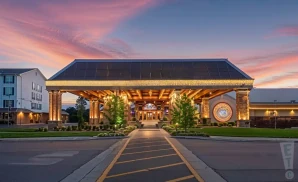 a hyper-realistic wide-angle aerial photograph of diamond jo casino in dubuque, iowa, captured at sunset with golden light casting warm highlights across the casino’s bold and industrial-style archite