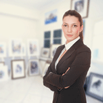 A curator stands confidently with arms crossed in an art gallery filled with framed artwork.