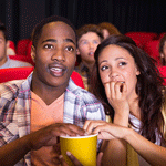 Two people sitting in a theater with rapt expressions, focused on the movie screen.