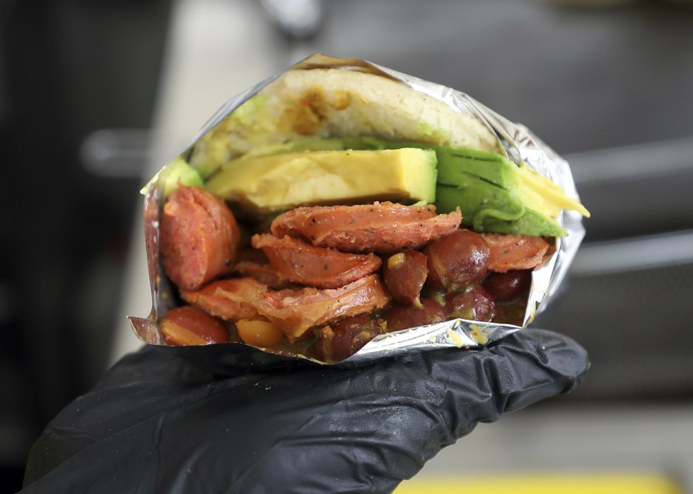 In this June 11, 2019 photo, a food server shows a Venezuelan arepa made with Colombian ingredients at the "Arepas Cafe" fast food restaurant in Bogota, Colombia. Venezuelans like to jest that their beloved arepas are so widely consumed that babies come out of the womb with the corn flatbreads already in hand. Now, as millions flee their homeland's turmoil, they are taking Venezuela's most ubiquitous dish with them.(AP Photo/Fernando Vergara) | FACTSWANTED
