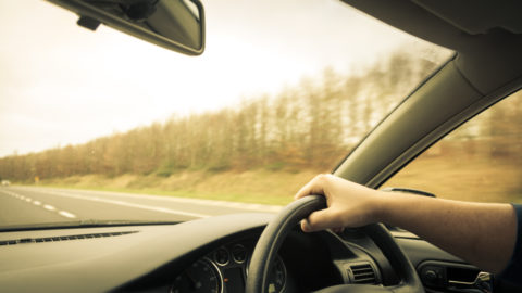 Male driver hands holding steering wheel of a car and road