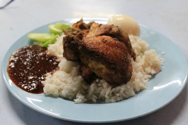 Traditional Nasi Lemak is a deep-fried chicken drumstick with a fried egg, chili paste, sliced cucumber, fried anchovies and peanuts
