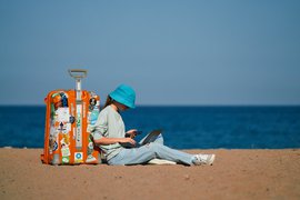 A woman sitting on a beach with a suitcase
