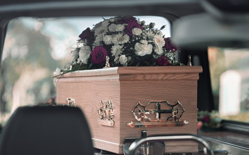 Flower-adorned casket in car’s back seat, symbolizing a final journey in Middletown, NJ.