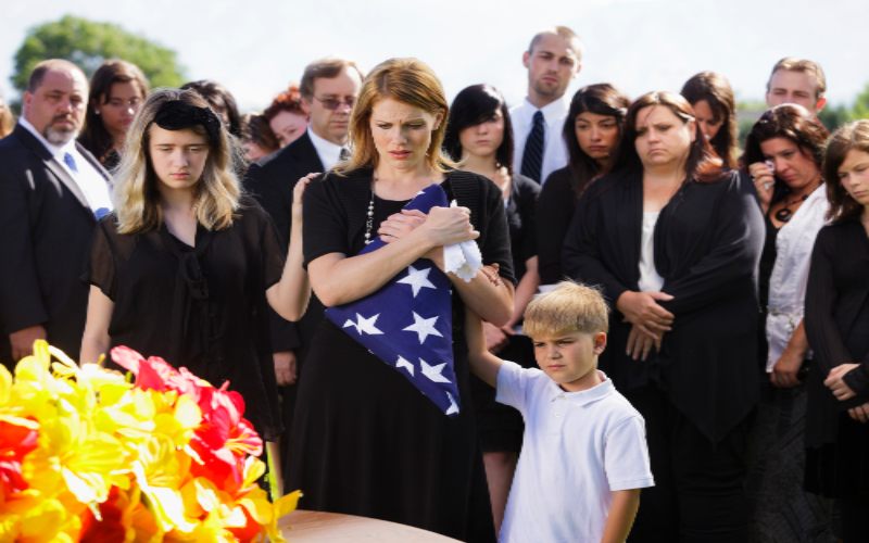 Woman with flag and child amid crowd, symbolizing unity and remembrance in Middletown funeral.