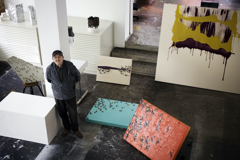 Color photographic portrait of Juan Genovés in his studio surrounded by paintings