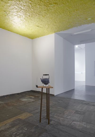 installation by pier paolo calzolari featuring a teapot on a wooden pedestal and a yellow, waxy ceiling