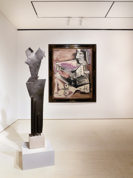 Image of the second floor which features a sculpture by Gonzalez in front of a painting by Pablo Picasso. The sculpture by Julio Gonzalez is titled "Femme dite les Trois Plis" and is made of bronze.