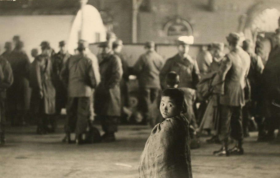Werner Bischof - Pusan, South Korean (Little Beggar among American soldiers in station at Pusan, Korea), 1952 Gelatin silver exhibition print mounted to masonite | Bruce Silverstein Gallery