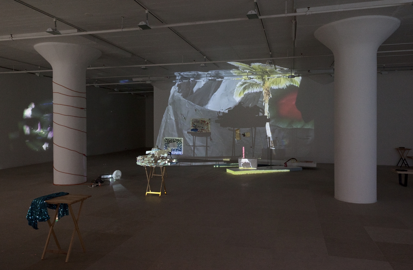 Bag's Circle, 2012, Single-channel video installation with four acrylic-on-canvas paintings, painted foam sculptures, CD rack, plastic cups, sticks, plexiglass, tape, clay, three folding tables, sequined throw, extendable fork, Continuous loop, Dimensions variable