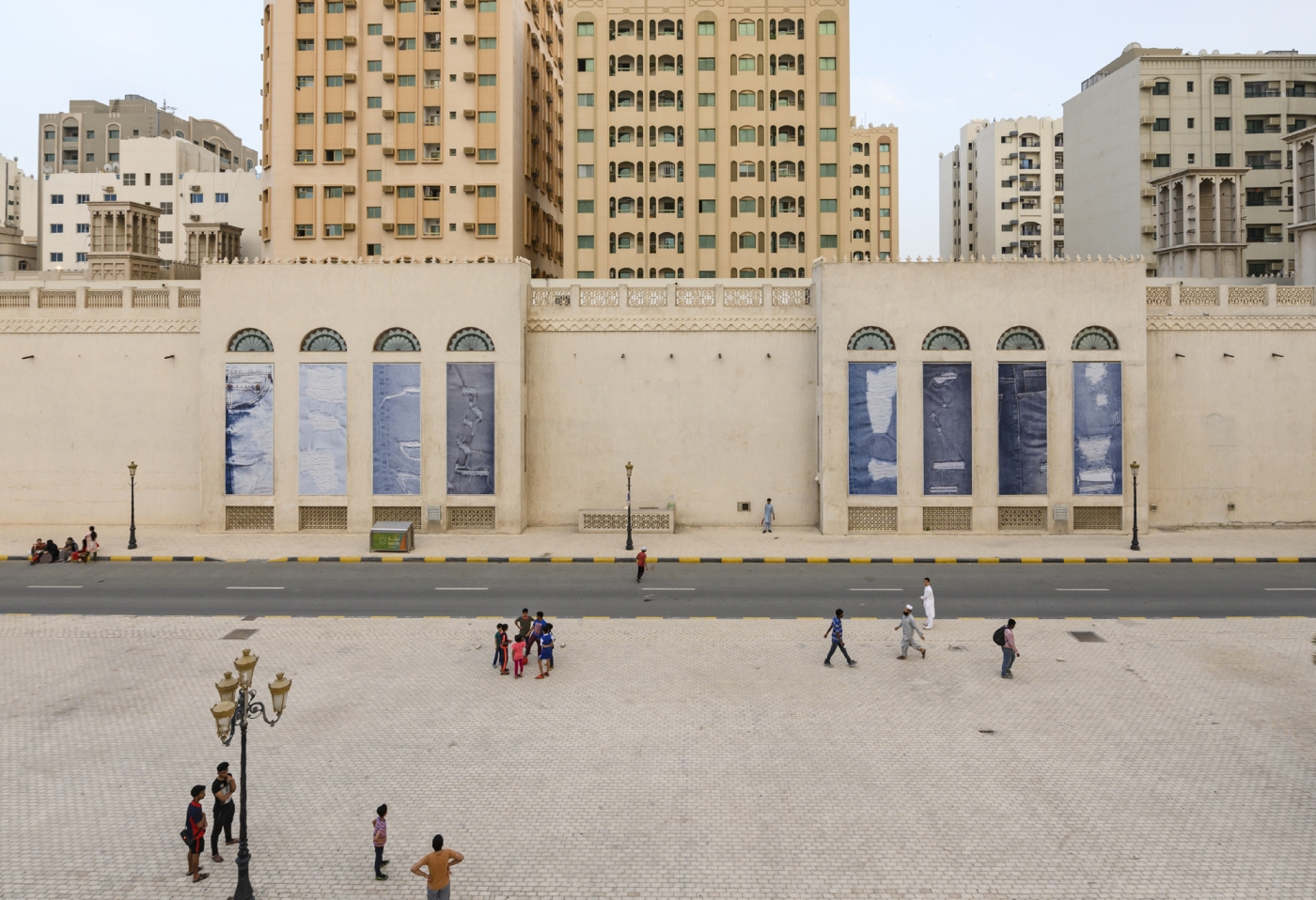 Eight vertical vinyl prints of textured denim arranged in panels along two concrete walls outdoors.