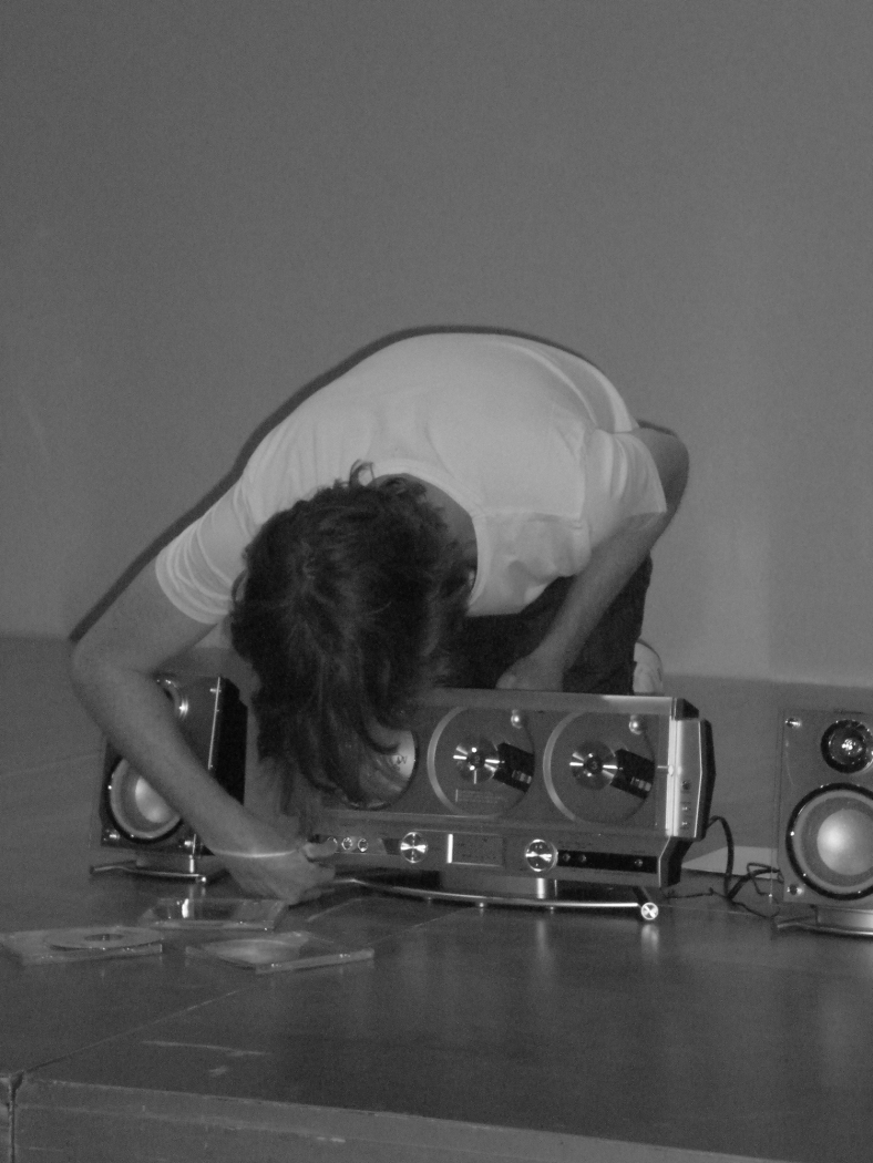A black and white image of Arcangel configuring a stereo system for his performance.