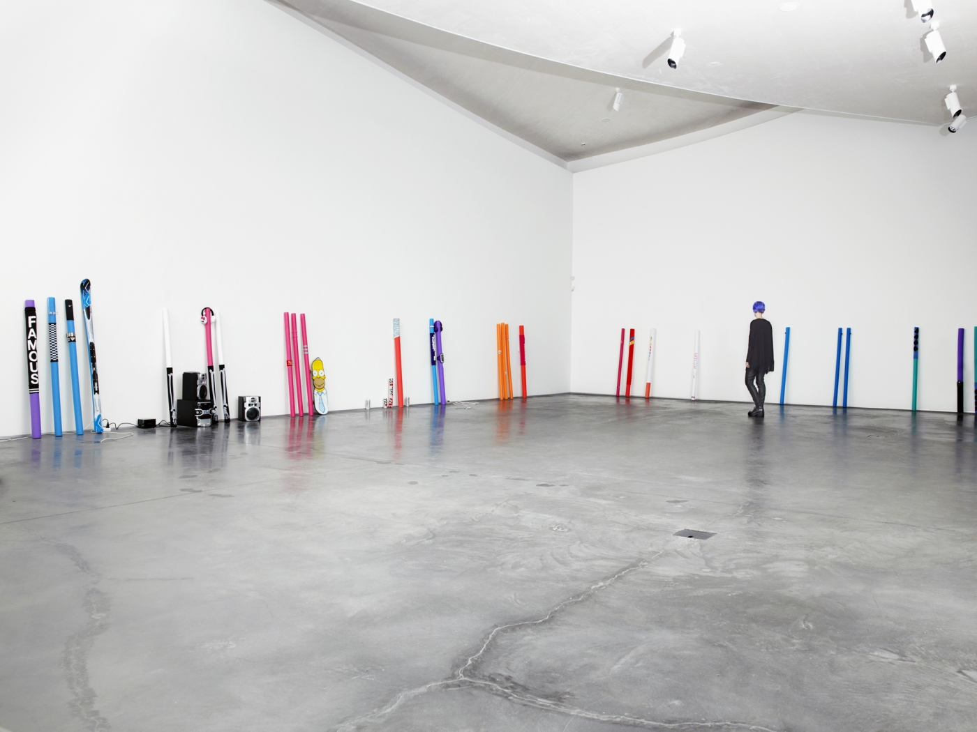 Multicolored skiis, hockey sticks, headphones, and a stereo set aligned upright along the bottom of two walls.