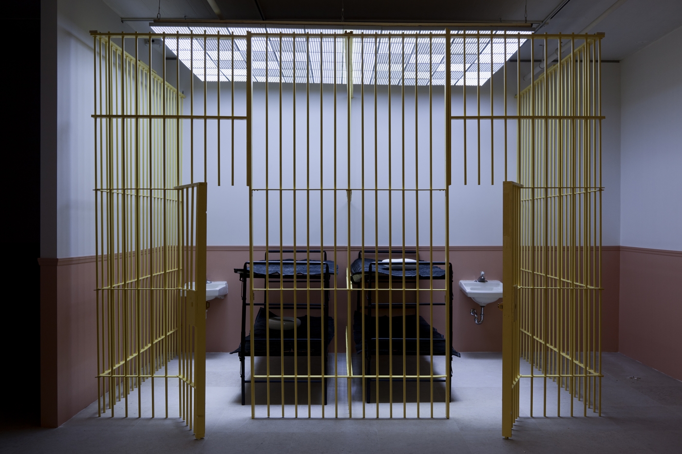 Tony Conrad WiP, 2013 Mixed media installation with wooden bars, locks, bunk beds, moving blankets, bed pans, sinks, overhead LED lighting, and video Dimensions variable