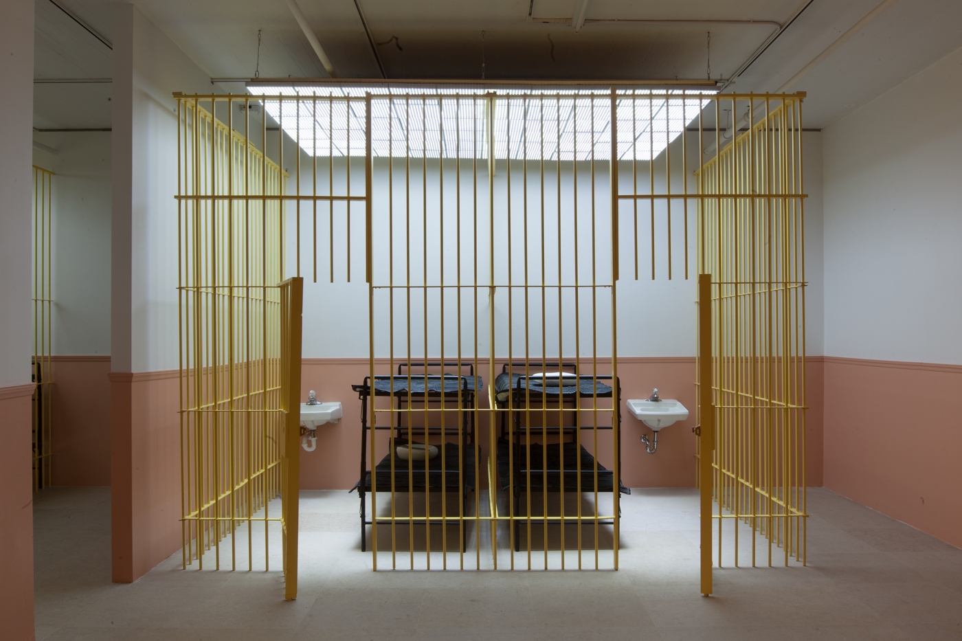 Tony Conrad, WiP, 2013, Mixed media installation with wooden bars, locks, bunk beds, moving blankets, bed pans, sinks, overhead LED lighting, and video, Dimensions variableTony Conrad WiP, 2013 Mixed media installation with wooden bars, locks, bunk beds, moving blankets, bed pans, sinks, overhead LED lighting, and video Dimensions variable