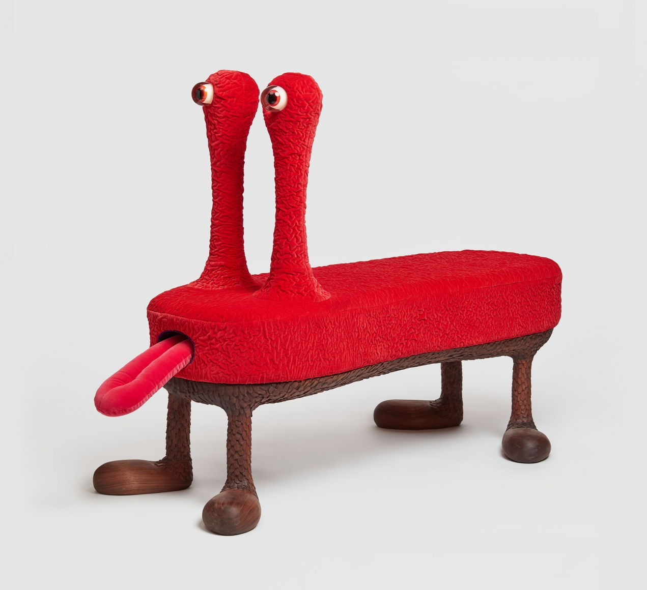 Red four legged bench sculpture with light up snail-like eyes and a retractable tongue by the artists the haas brothers