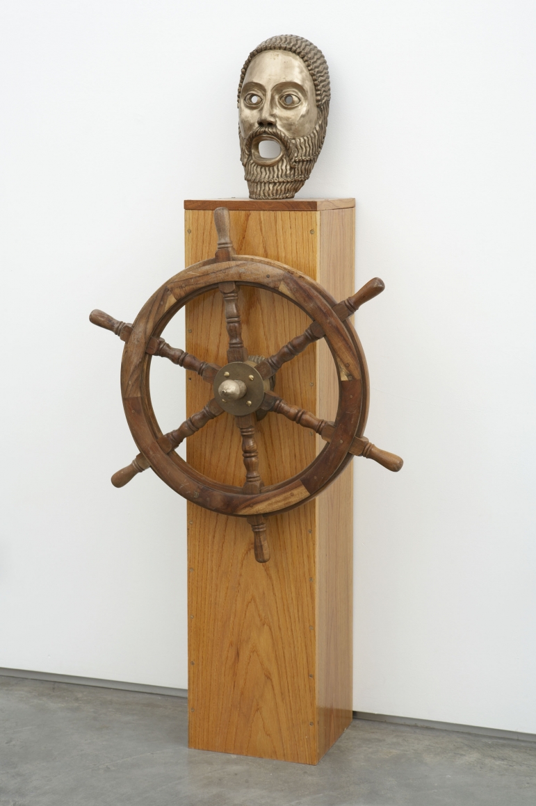 sculpture with wheel and mask on wooden pedestal by pentti monkkonen