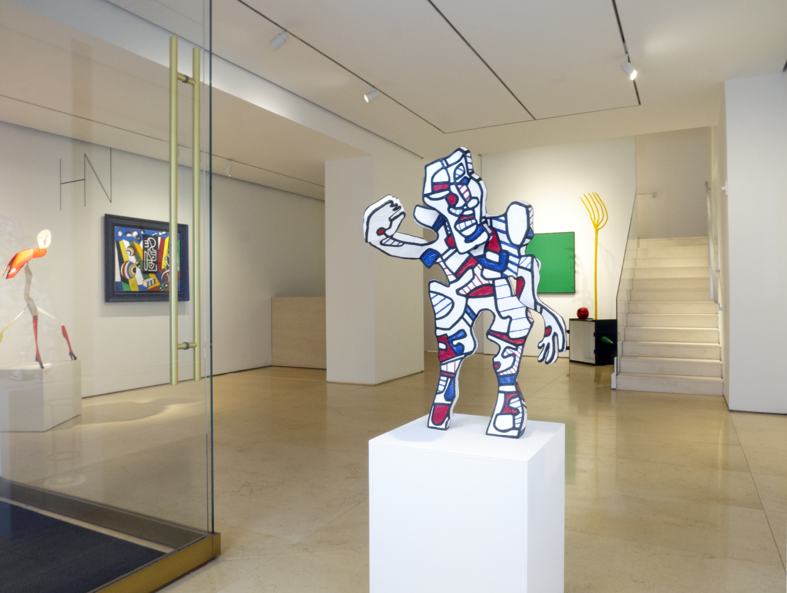 Installation view of Masterworks. View of the lobby entrance featuring a medium size sculpture by French sculptor, painter Jean Dubuffet. The sculpture is titled (The Welcomin) L'Acceuillant and was made in 1973. It represents a human shape standing and waiving with its right arm. The sculpture is overall white but is covered with thick blacl lines, red and blue spots and stripes that define in a simple way the face of this figure. This style is the famous Hourloupe signature style that Dubuffet used in many of his paintings and sculptures.
