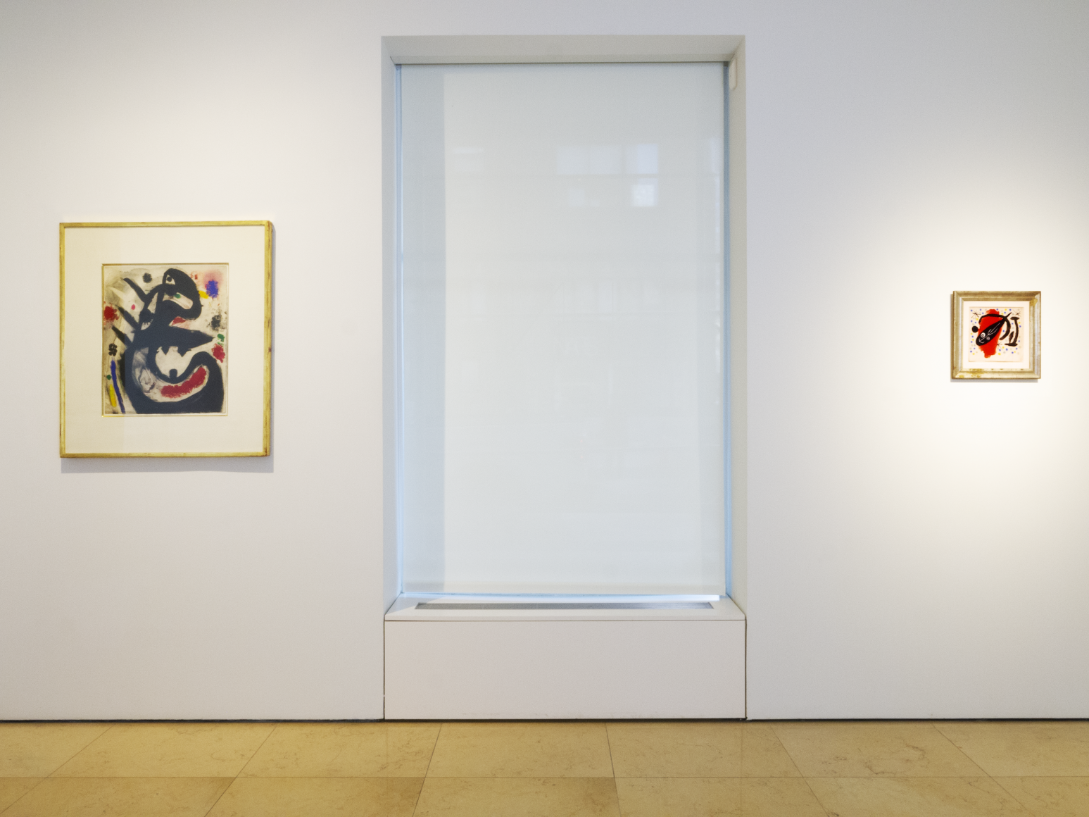 Installation view of Masterworks. This image features two watercolors by Joan Miro the Spanish painter. On the left a medium size watercolors represent a large head painted in black with a mouth open wide and a lively expression. On the right ot os the cover of a poetry magazine, representing a black fish over. a red spot.