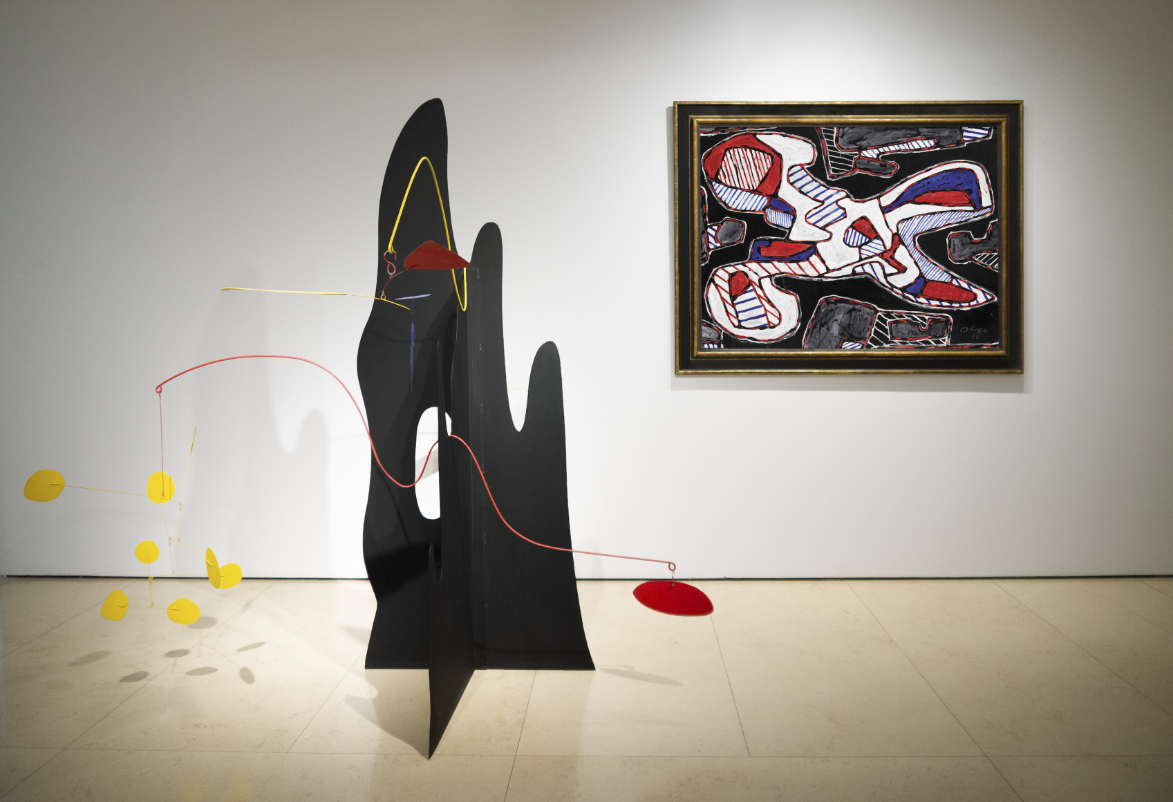 this is an image featuring the lobby entrance of Helly Nahmad Gallery featuring a stabile sculpture by Alexander Calder and a painting by Jean Dubuffet. Calder sculpture is Crag with Petals and Yellow Cascade, produced in 1974. It is made black sheet metal. The sculpture's base looks like a mountainous form it is composed of two sheets. The sculpture features two undulating metal stems balanced in the cavities and peaks of this mountainous form, disrupting the dense and static plinth and allowing light polychromatic elements to swirl and catch the air. The painting by jean Dubuffet is titled "Ciseaux I" (scissors I) and was produced in 1966. Redefining the traditional genre of still life objects such as scissors tea cups and kitchen stove with his hour loupe signature style, Dubuffet painted a large scale pair of scissors flattened into a two dimensional aerial perspective and rendered with interlocking blue and red stripes over an abstracted black background.
