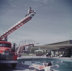 Slim Aarons, To Any Lengths, 1954: Slim Aarons photographing Mara Lane from the top of an extending ladder by the swimming pool at Sands Hotel, Las Vegas