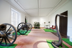 "Décor: A Conquest" (XIXth Century Room), 1975, One flower ball on wooden pedestal, ten grass mats, eight palm trees, one colour photograph of a cowboy film, two wooden barrels (labeled ‘GIN’ and ‘RUM’), two silver-plated candelabras on two iron plinths with wooden tops, two red velvet Edwardian chairs, four light reflectors (one red and three green), one stuffed python, one XIXth-century pistol on wooden pedestal, one circular table with green felt displaying one miniature pack of cards, one plastic crab, and one plastic lobster, two Waterloo-style cannons.