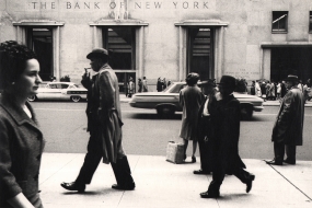 Simpson Kalisher, Untitled, c. 1959. Pedestrians walk horizontally across the frame on a sidewalk across the street from the Bank of New York, seen in the background.
