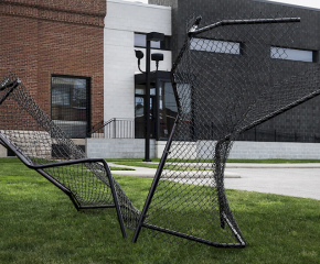 Black chain link fence sculpture jutting out of grass